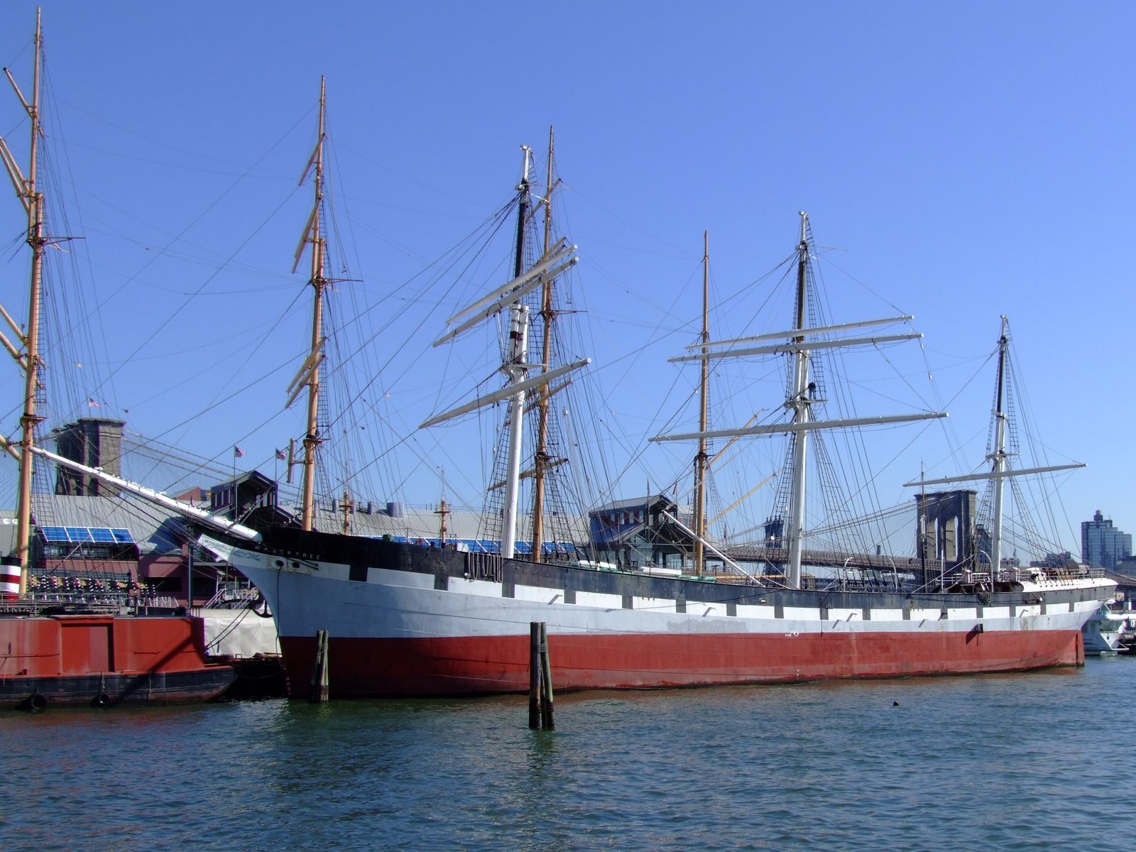 A tall ship moored at South Street Seaport with the Brooklyn Bridge behind it